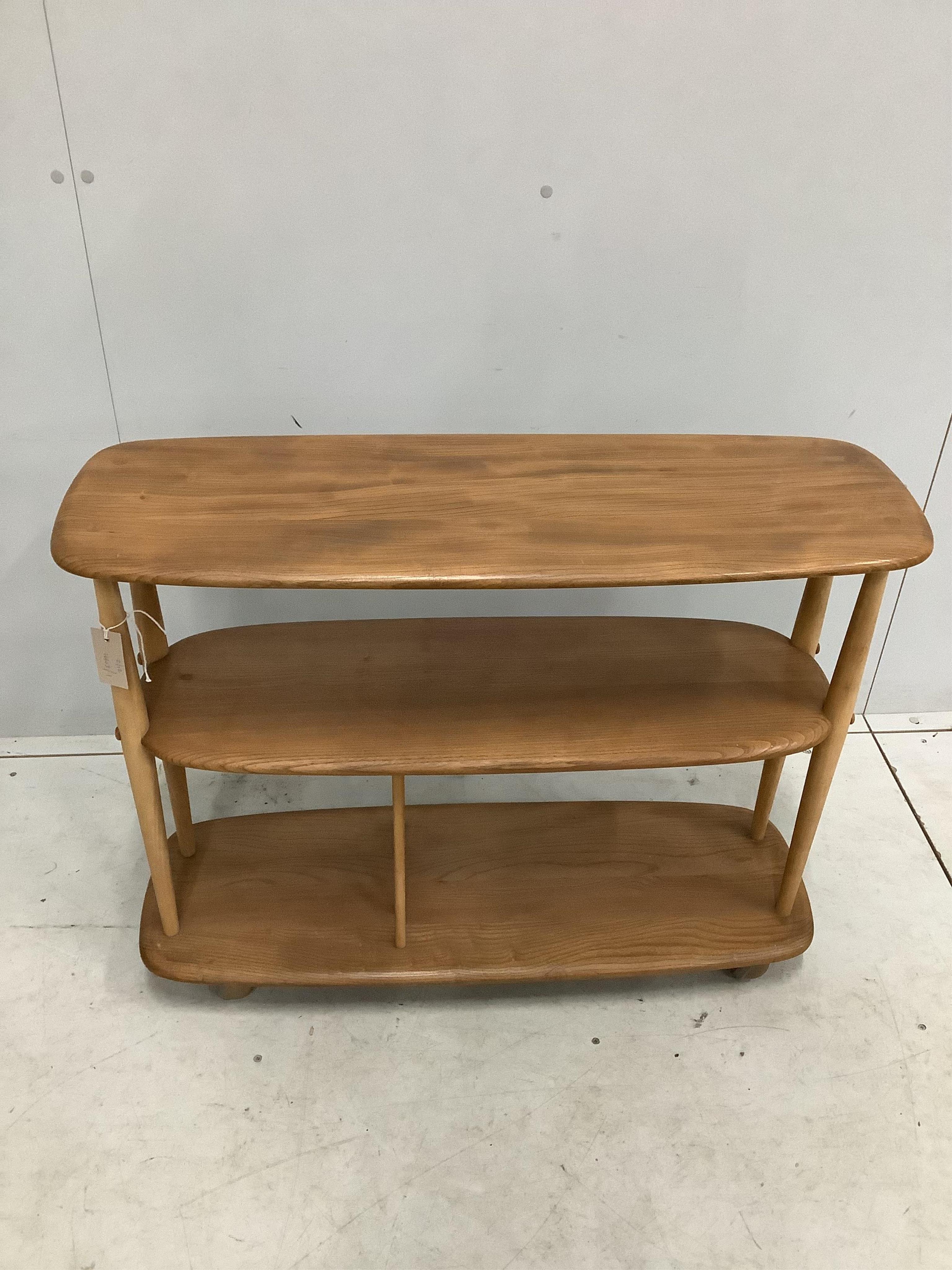 An Ercol Windsor elm and beech three tier book trolley, model 361. Width 91cm, depth 32cm, height 71cm. Condition fair to good, a little sun faded.